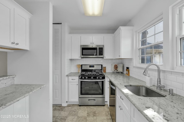 kitchen featuring appliances with stainless steel finishes, light stone counters, white cabinets, backsplash, and sink