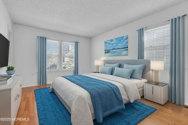 bedroom featuring a textured ceiling, light hardwood / wood-style flooring, and multiple windows