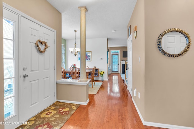 entryway with a textured ceiling, a notable chandelier, ornate columns, and hardwood / wood-style flooring