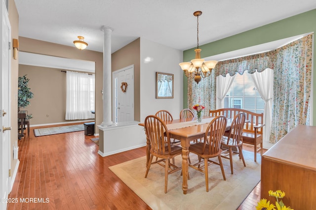 dining room with light wood-type flooring, a textured ceiling, a chandelier, and decorative columns