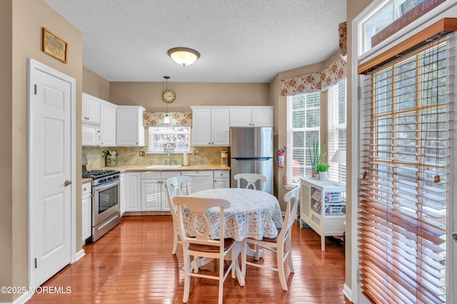 kitchen with white cabinetry, stainless steel appliances, decorative backsplash, decorative light fixtures, and light wood-type flooring