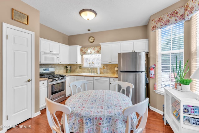 kitchen featuring stainless steel appliances, tasteful backsplash, decorative light fixtures, white cabinets, and sink