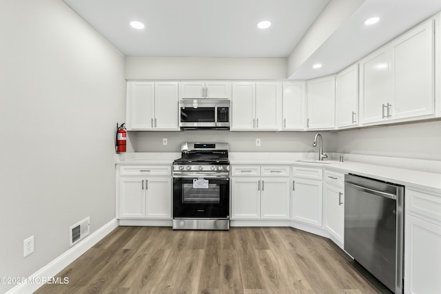 kitchen featuring appliances with stainless steel finishes, light hardwood / wood-style floors, white cabinets, and sink