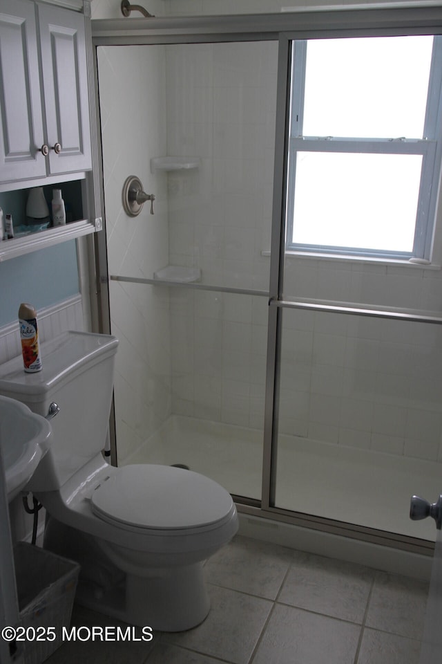 bathroom featuring toilet, tile patterned flooring, a shower with shower door, and a wealth of natural light