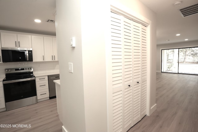 kitchen with white cabinets, appliances with stainless steel finishes, light hardwood / wood-style floors, and backsplash