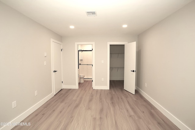 unfurnished bedroom featuring a spacious closet, light wood-type flooring, a closet, and ensuite bath