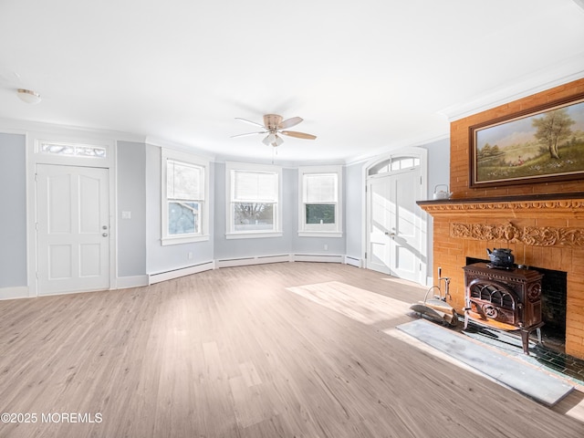 unfurnished living room with a wood stove, ceiling fan, ornamental molding, light wood-type flooring, and a baseboard radiator