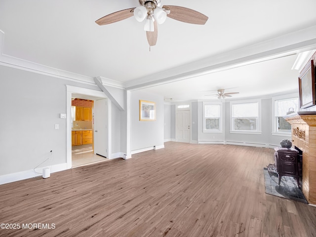 unfurnished living room featuring ornamental molding, ceiling fan, a wood stove, and hardwood / wood-style flooring