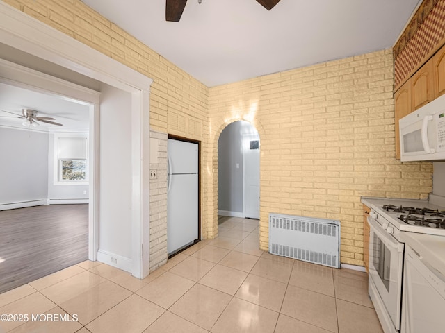 kitchen featuring white appliances, light tile patterned flooring, brick wall, and radiator