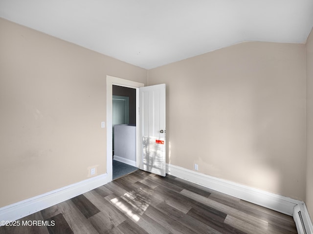 empty room featuring a baseboard heating unit, vaulted ceiling, and dark wood-type flooring