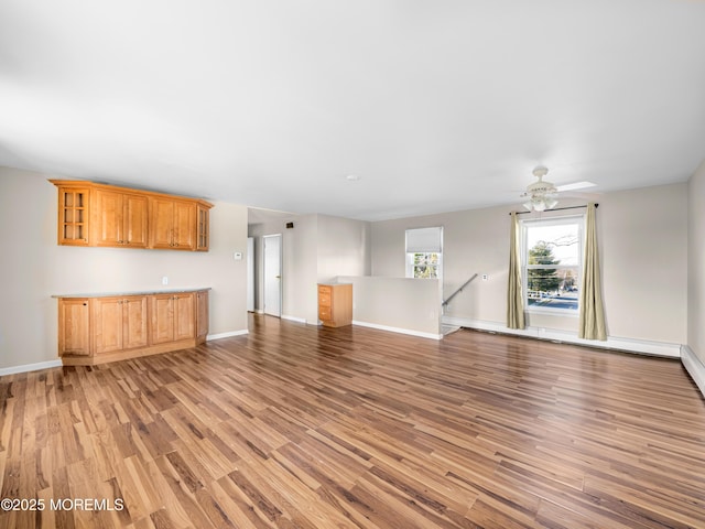 unfurnished living room featuring a baseboard heating unit, light wood-type flooring, and ceiling fan