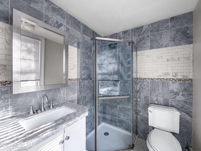 bathroom with tile walls, a shower with shower door, vanity, and toilet