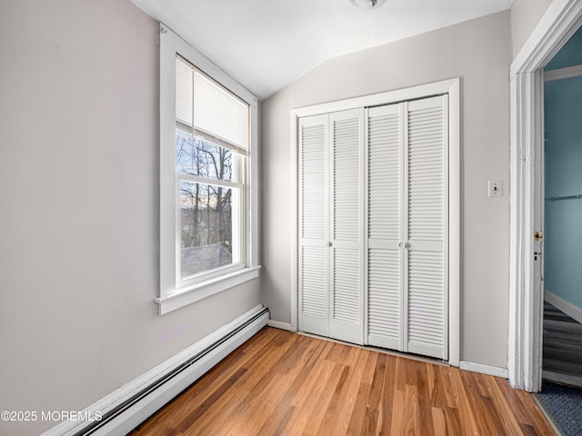 unfurnished bedroom with lofted ceiling, a baseboard radiator, a closet, and hardwood / wood-style floors