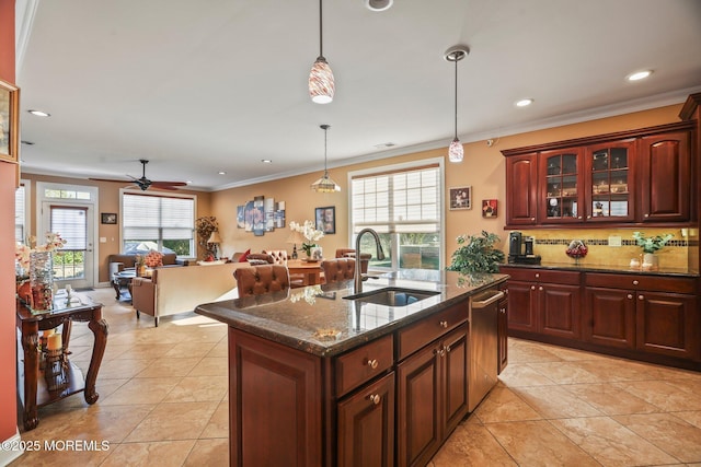 kitchen featuring dark stone counters, sink, hanging light fixtures, a kitchen island with sink, and ceiling fan