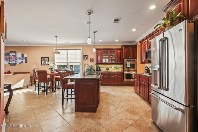 kitchen featuring appliances with stainless steel finishes, a kitchen island with sink, light tile patterned flooring, ornamental molding, and a breakfast bar