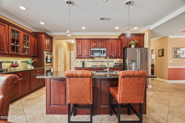 kitchen with appliances with stainless steel finishes, pendant lighting, dark stone countertops, and an island with sink