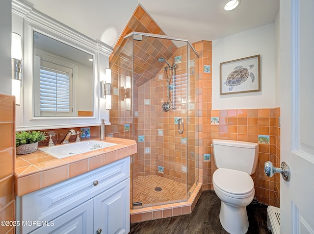 bathroom with toilet, vanity, tile walls, a shower with shower door, and a baseboard heating unit