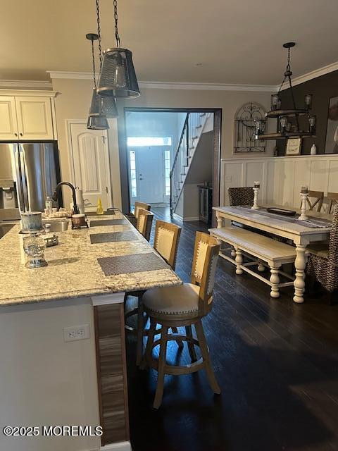 kitchen with pendant lighting, ornamental molding, stainless steel fridge with ice dispenser, and a breakfast bar area