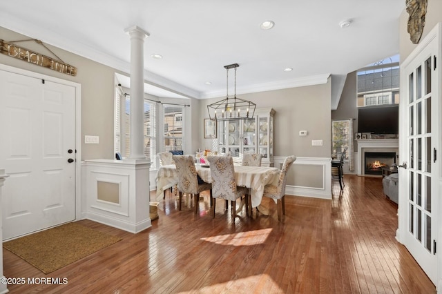 dining area with ornate columns, crown molding, hardwood / wood-style floors, and an inviting chandelier