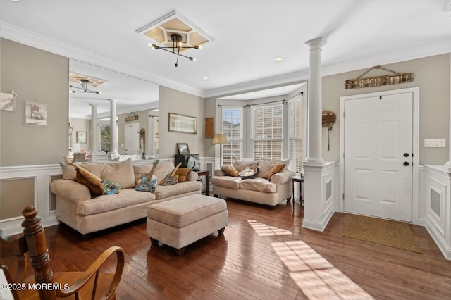 living room featuring dark wood-type flooring, ornamental molding, a chandelier, and decorative columns