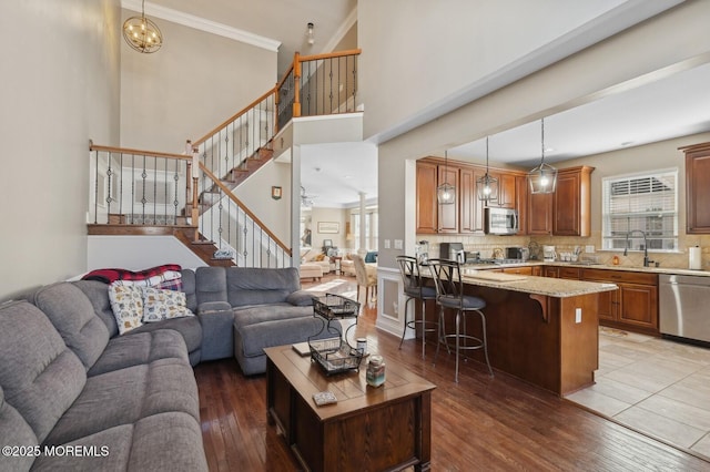 living room featuring dark wood-type flooring, ornamental molding, ceiling fan with notable chandelier, and sink