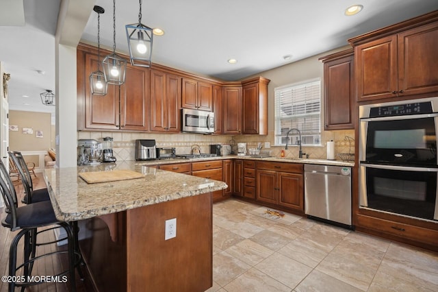 kitchen featuring a kitchen bar, kitchen peninsula, appliances with stainless steel finishes, decorative light fixtures, and light stone countertops