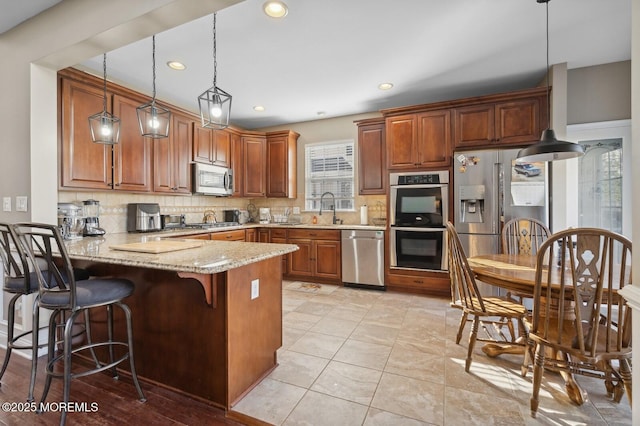 kitchen with kitchen peninsula, stainless steel appliances, decorative light fixtures, light stone countertops, and sink