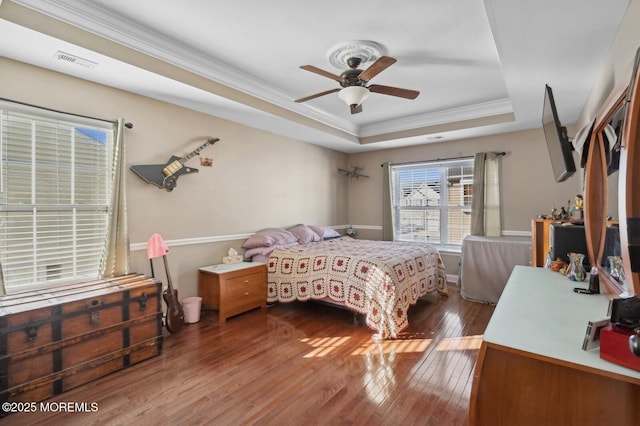 bedroom featuring ceiling fan, wood-type flooring, a raised ceiling, and crown molding