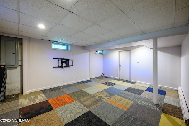 basement with a paneled ceiling, electric panel, and baseboard heating