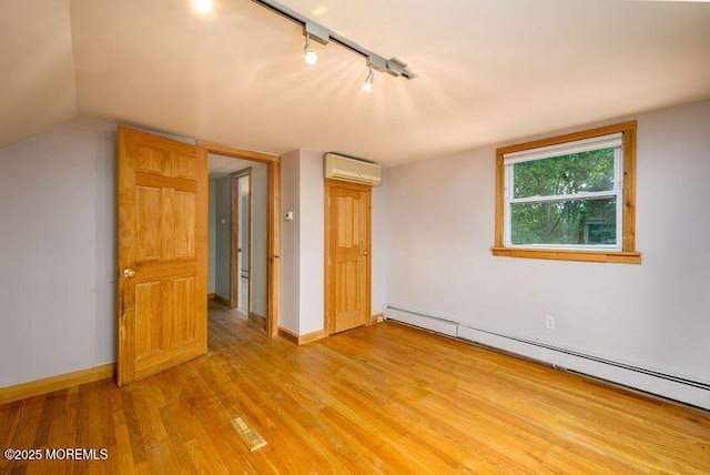 unfurnished bedroom featuring rail lighting, a wall mounted air conditioner, light hardwood / wood-style flooring, a baseboard heating unit, and lofted ceiling