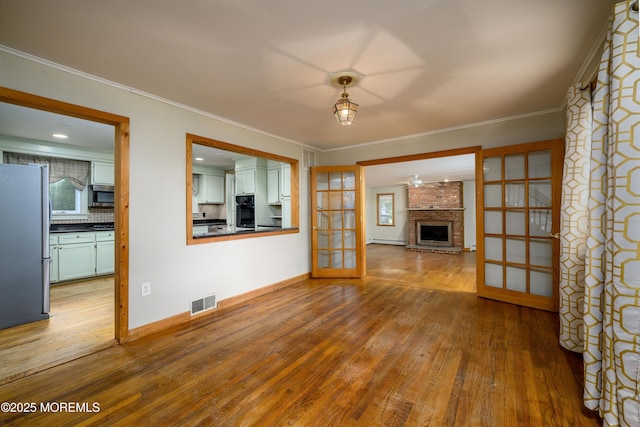 unfurnished living room with a brick fireplace, light wood-type flooring, crown molding, and french doors