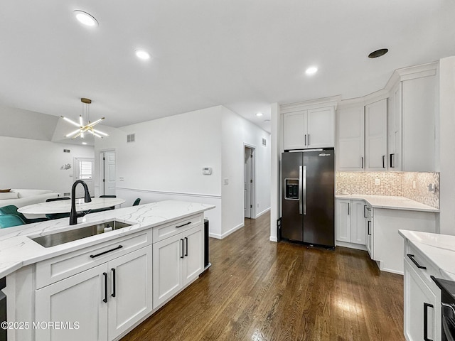 kitchen with white cabinetry, stainless steel fridge, sink, and light stone counters