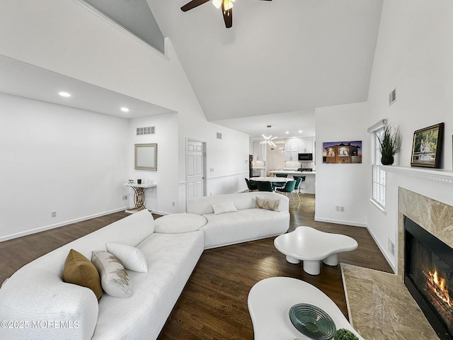 living room featuring a fireplace, high vaulted ceiling, ceiling fan, and dark wood-type flooring