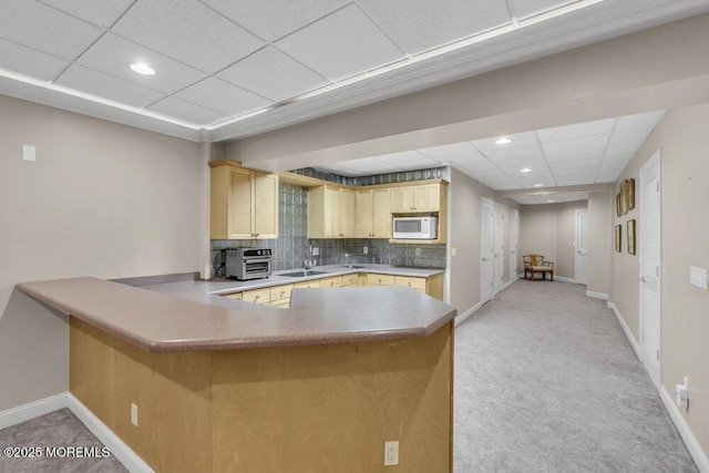 kitchen with sink, a drop ceiling, kitchen peninsula, light brown cabinetry, and backsplash