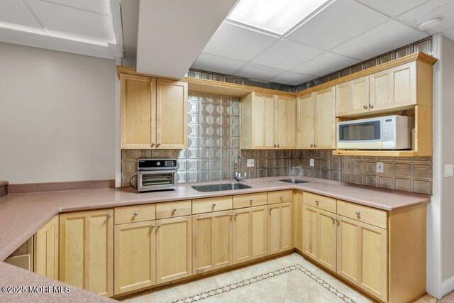 kitchen featuring sink, a drop ceiling, light tile patterned floors, light brown cabinetry, and backsplash