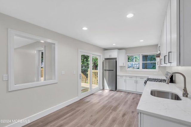 kitchen featuring light stone countertops, white cabinetry, sink, and stainless steel refrigerator