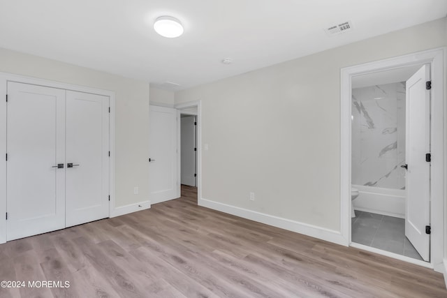 unfurnished bedroom featuring connected bathroom, a closet, and light wood-type flooring