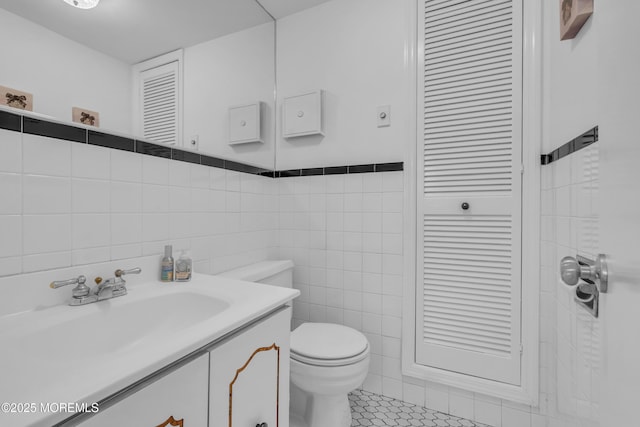 bathroom with tile walls, toilet, vanity, and tile patterned flooring