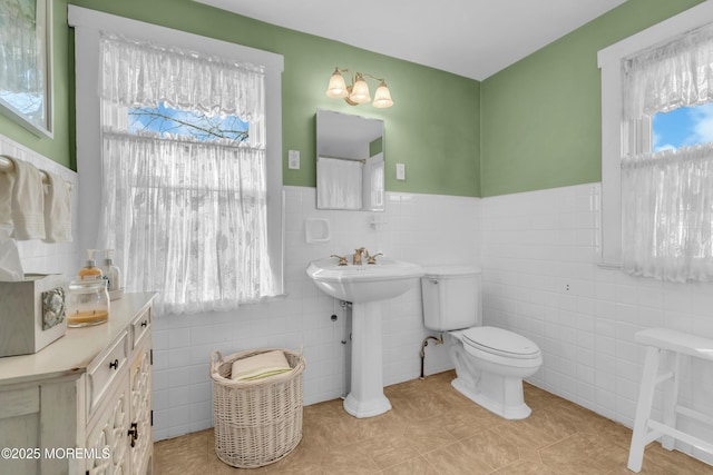 bathroom with toilet, tile patterned flooring, tile walls, and plenty of natural light