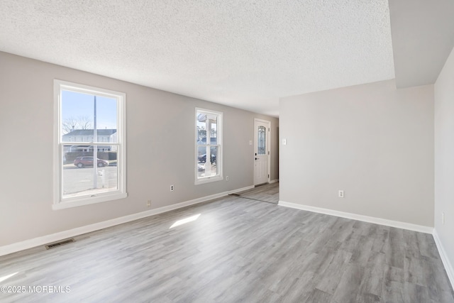 spare room with a wealth of natural light, a textured ceiling, and light hardwood / wood-style floors