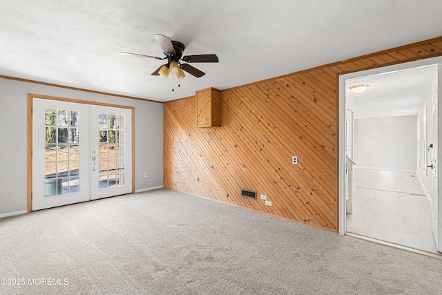 unfurnished room with ceiling fan, carpet floors, french doors, and wooden walls