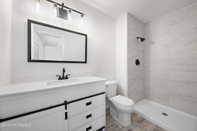 bathroom with a tile shower, vanity, and toilet