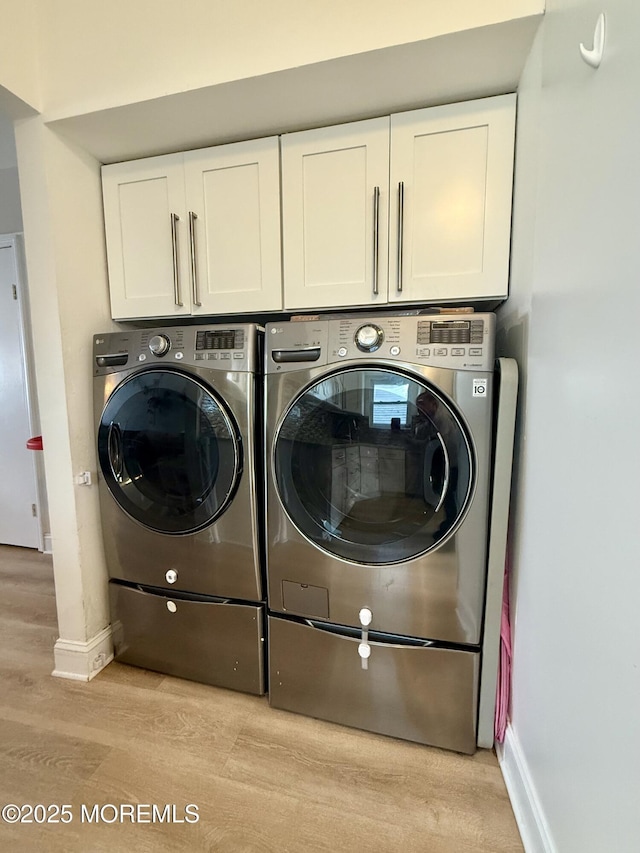 laundry room with washing machine and dryer, cabinets, and light hardwood / wood-style floors