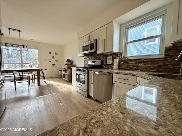 kitchen featuring stone counters, white cabinets, decorative backsplash, appliances with stainless steel finishes, and decorative light fixtures