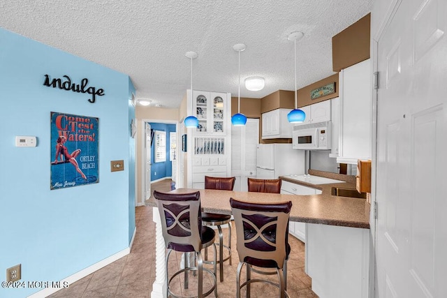 kitchen featuring white appliances, light tile patterned floors, a textured ceiling, white cabinets, and decorative light fixtures