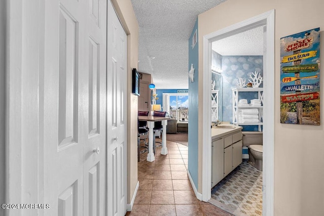 hall with a textured ceiling, light tile patterned flooring, and sink