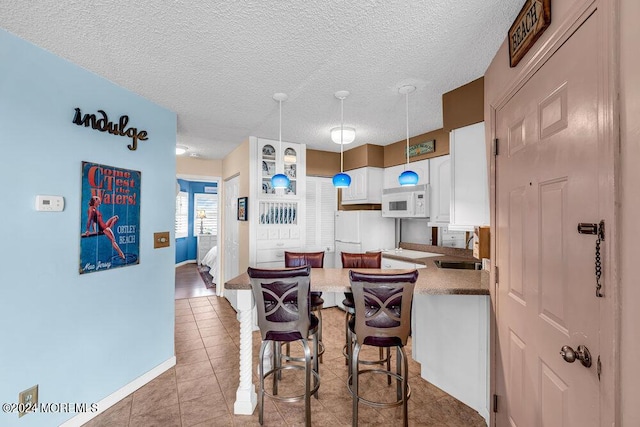 kitchen featuring white appliances, hanging light fixtures, light tile patterned floors, sink, and white cabinetry