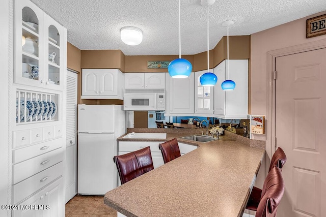 kitchen featuring white appliances, decorative light fixtures, a kitchen breakfast bar, and sink