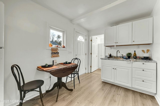 kitchen with sink, light wood-type flooring, beam ceiling, and white cabinetry