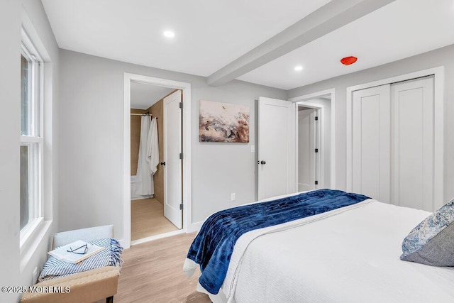 bedroom featuring a closet, light hardwood / wood-style flooring, beamed ceiling, and connected bathroom